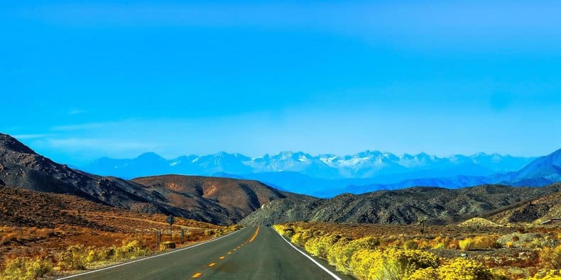 Driving down road toward mountains on horizon with bright blue sky