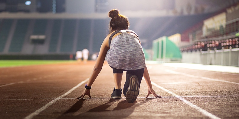 Happy young female athlete set at a starting position for running in stadium at night