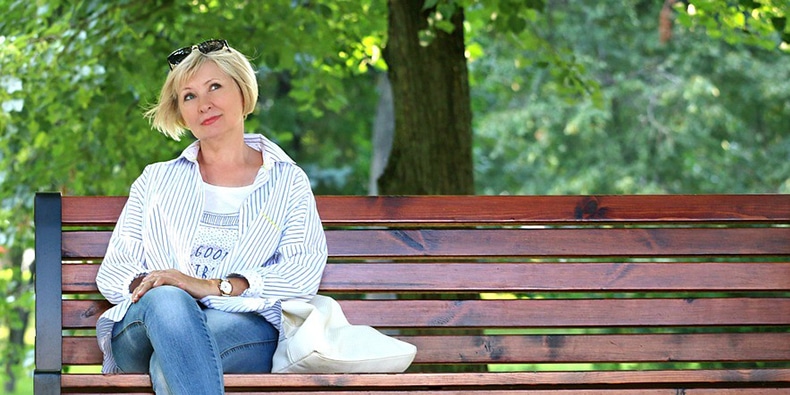 Blonde woman with sunglasses sitting on bench and thinking in park