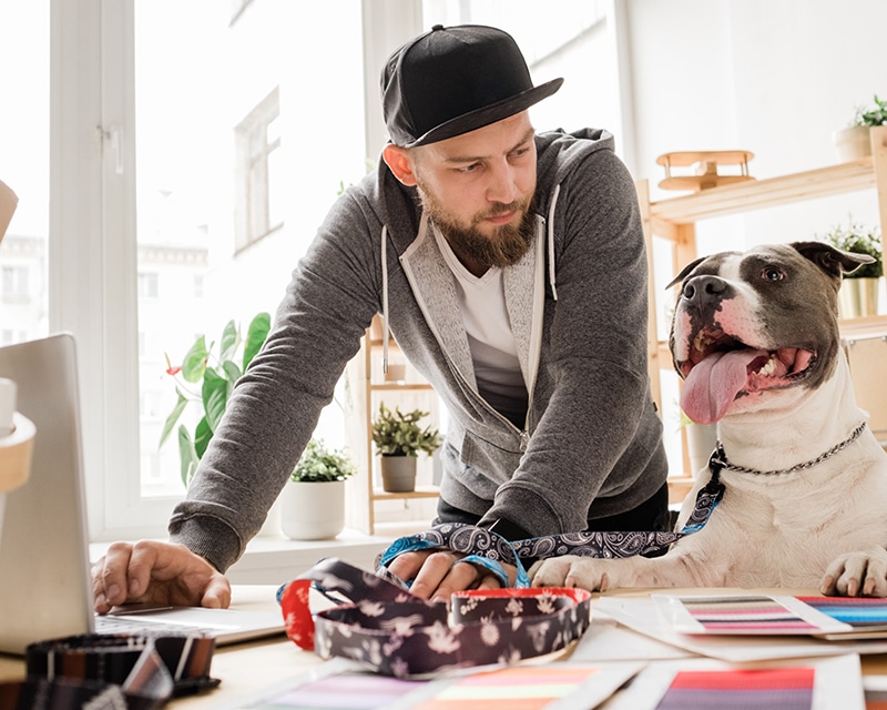 Young casual man looking at his dog while bending over workplace