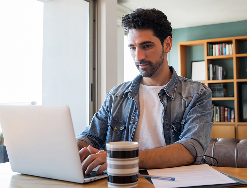 Business man working with laptop from home. Portrait of young man working with a laptop from home while woman talking on phone at background. Home office concept. New normal lifestyle.