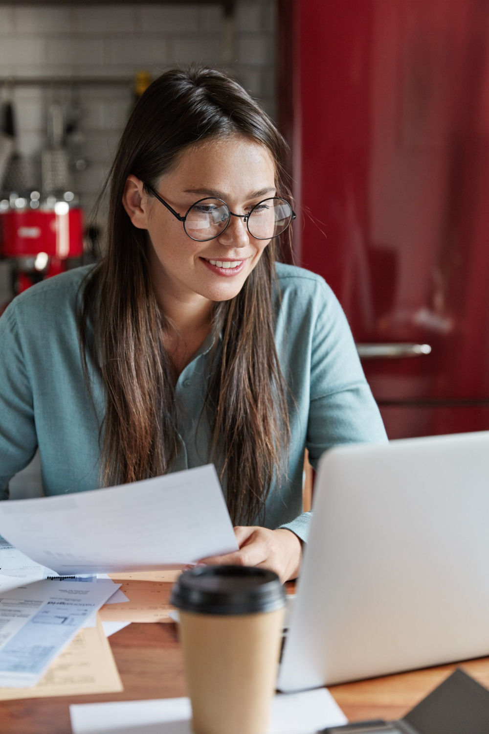 delighted-pleased-young-woman-creats-successful-plan-banking-holds-paper-documents-looks-positively-laptop-computer-sits-kitchen-table (1)