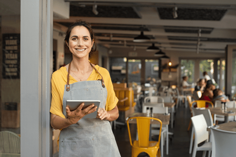 Young woman holding an ipad in front of her business | Lean Solutions: Transform your Business into a Lean Mean Business Machine