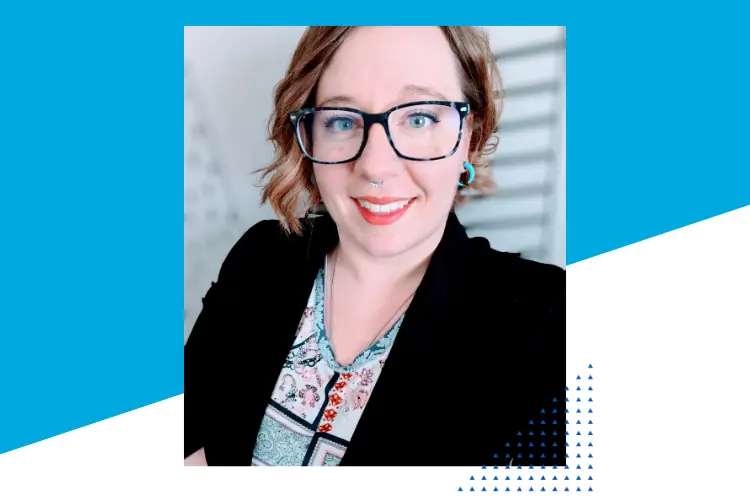 A professional woman with short wavy hair, wearing blue-framed glasses, a nose ring, and turquoise earrings. She is dressed in a black blazer over a patterned blouse, smiling confidently at the camera. The background features a modern, lightly blurred setting with blue and white geometric accents on the image border