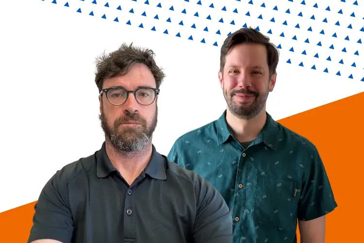 Two men standing in front of a graphic background with orange and blue geometric shapes. One man has curly dark hair, a beard, and glasses, wearing a black polo shirt. The other man has short dark hair and a trimmed beard, wearing a green button-up shirt with a subtle pattern. Both are facing the camera and smiling slightly.